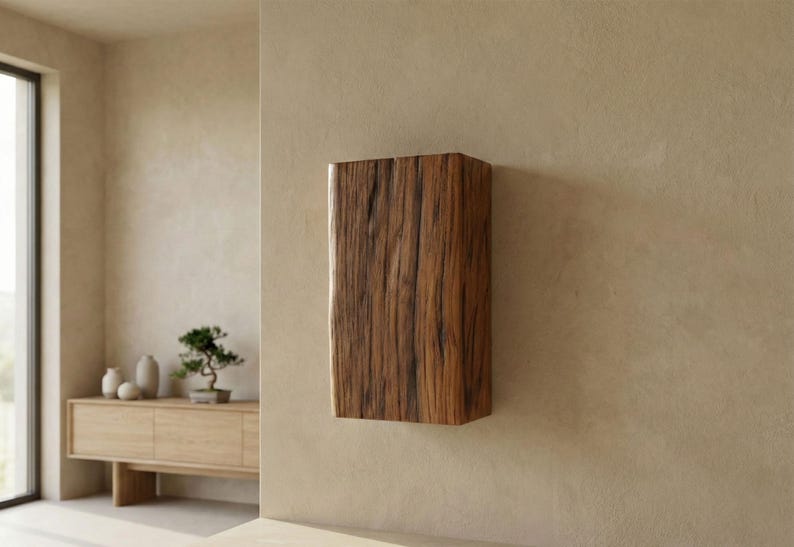 May include: A rectangular, wall-mounted cabinet made of dark brown wood with visible grain. The cabinet is the focal point, mounted on a beige wall. The room has a minimalist design with a wooden sideboard and a bonsai tree.