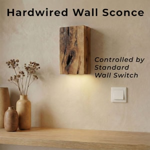 May include: A hardwired wall sconce made of a rectangular block of wood with a natural grain pattern. The sconce is illuminated from the bottom and controlled by a standard wall switch. The text "Hardwired Wall Sconce" is at the top.