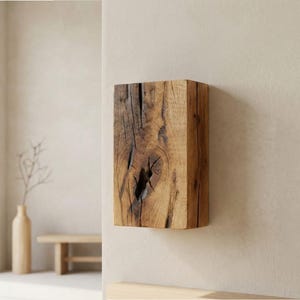 May include: A rectangular, solid wood block with a natural, weathered appearance. The wood grain and knots are visible, showcasing the natural texture and color variations of the material. The block is mounted on a neutral-colored wall, suggesting a decorative or functional item.