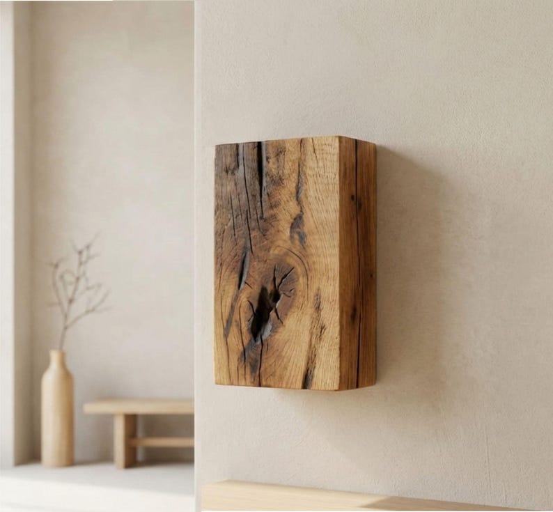 May include: A rectangular, solid wood block with a natural, weathered appearance. The wood grain and knots are visible, showcasing the natural texture and color variations of the material. The block is mounted on a neutral-colored wall, suggesting a decorative or functional item.