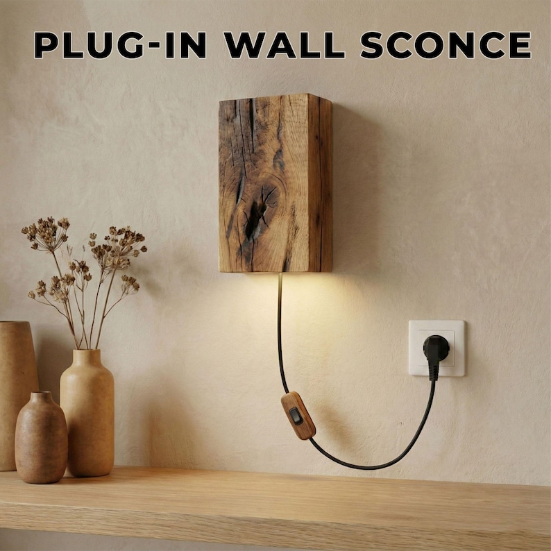 May include: A plug-in wall sconce made from a rectangular block of wood with a natural grain pattern. The sconce has a warm light emanating from the bottom. A black cord with a wooden switch and plug extends to a wall outlet. The text "PLUG-IN WALL SCONCE" is at the top.