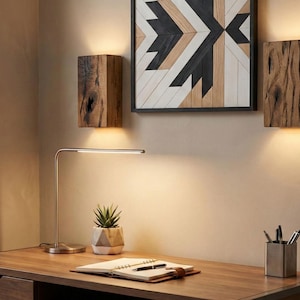 May include: A modern desk setup with a wooden desk, a silver desk lamp, and a small succulent in a geometric pot. Two wooden wall sconces and a framed geometric artwork are mounted on the wall above the desk.