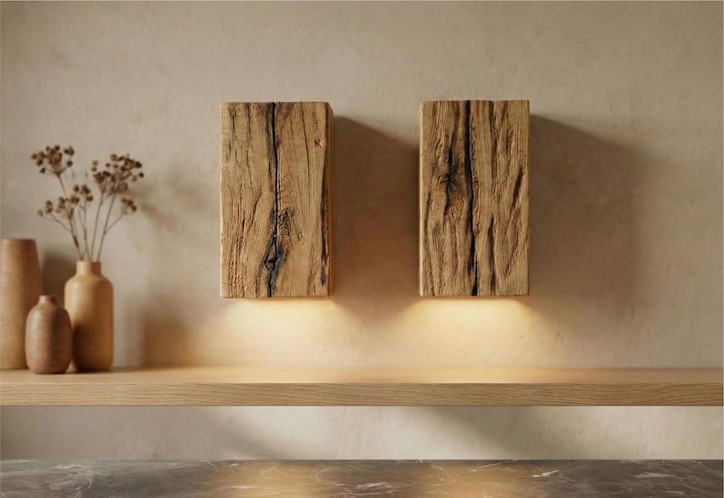May include: Two rectangular wooden wall sconces with a natural, weathered appearance. The sconces are mounted on a light-colored wall and emit a warm, inviting glow from the bottom. The wood grain and texture are prominent.