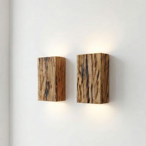 May include: Two wooden wall sconces with a natural, textured appearance. The sconces are rectangular and emit a warm light from the bottom. The wood has a mix of light and dark brown tones, creating a rustic aesthetic.
