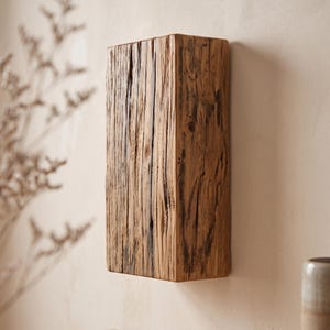 Può includere: Un blocco di legno rettangolare montato a parete con una superficie strutturata e usurata. Il legno presenta venature verticali pronunciate, fessure profonde e una finitura naturale marrone medio con striature scure.