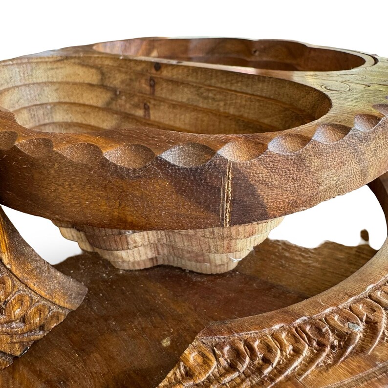 Peut inclure: Un panier &agrave; fruits en bois fait &agrave; la main avec une finition naturelle. Le panier pr&eacute;sente un design &agrave; plusieurs niveaux avec des d&eacute;tails sculpt&eacute;s et un bord festonn&eacute;. Le grain du bois est visible, ajoutant &agrave; son charme rustique. Le panier est con&ccedil;u pour contenir des fruits ou d'autres articles.