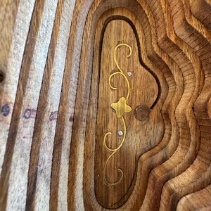 Peut inclure: Gros plan sur un bol d&eacute;coratif en bois avec un design en couches. Le bol pr&eacute;sente une incrustation florale dor&eacute;e avec de petits accents scintillants. Le bois a une teinte chaude et naturelle avec un grain visible.