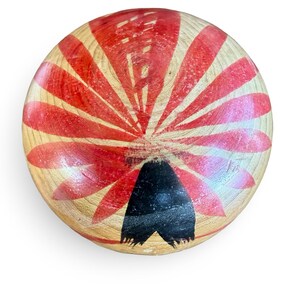 Peut inclure: Un objet circulaire en bois avec une finition naturelle au grain brun clair. La surface pr&eacute;sente un motif peint de p&eacute;tales ou de rayons rouges rayonnants partant du centre, avec une forme triangulaire noire solide sur le bord inf&eacute;rieur.