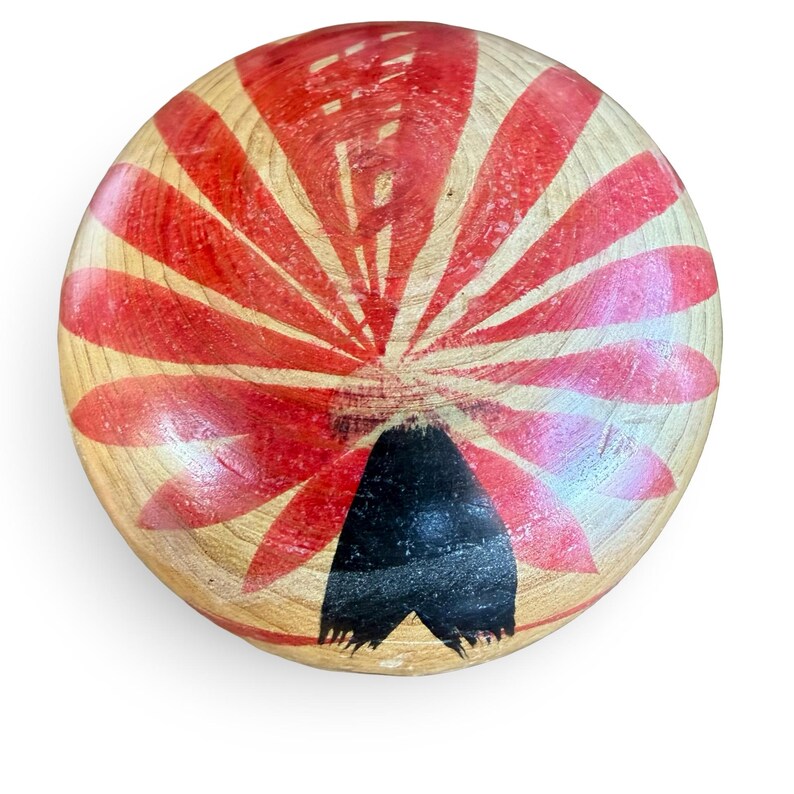 Peut inclure: Un objet circulaire en bois avec une finition naturelle au grain brun clair. La surface pr&eacute;sente un motif peint de p&eacute;tales ou de rayons rouges rayonnants partant du centre, avec une forme triangulaire noire solide sur le bord inf&eacute;rieur.