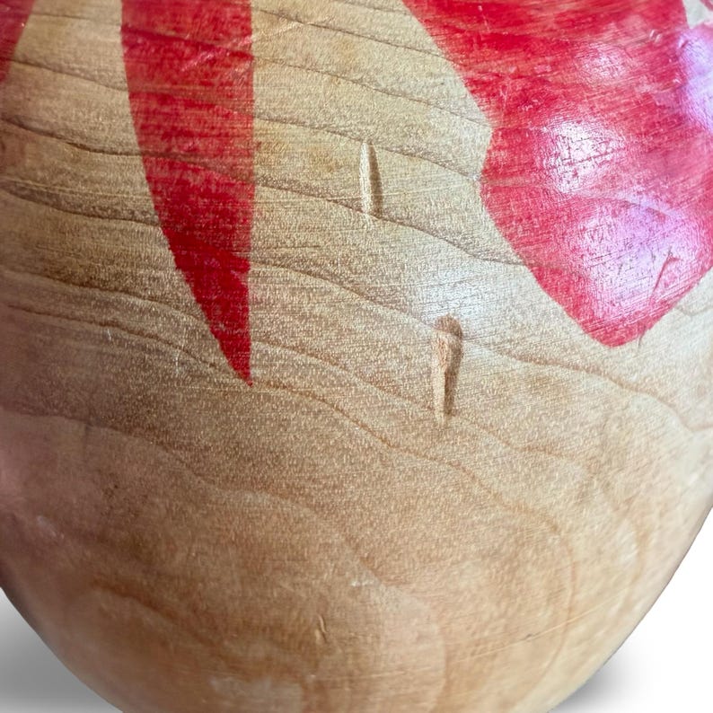 Peut inclure: Une vue rapproch&eacute;e d'un objet en bois clair et lisse pr&eacute;sentant un grain naturel et des sections peintes en rouge vif. La surface montre une texture de bois visible avec de l&eacute;g&egrave;res indentations et une finition polie sur la forme courbe.
