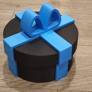 Puede incluir: Una caja de regalo redonda negra con un diseño de lazo y cinta azul brillante. La caja tiene una superficie texturizada y está sobre una superficie de madera. El texto en la imagen dice "IMPORTANT Digital Files Only! You need a 3D printer to print this product."