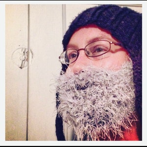 May include: A person wearing a blue knitted hat and a fluffy white beard. The person is wearing glasses and looking to the side.