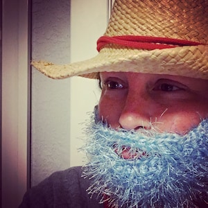 Puede incluir: Una persona con un sombrero de vaquero de paja con una banda roja y una barba azul y peluda.