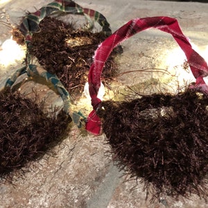 May include: Three brown fuzzy beard ornaments with plaid and red fabric accents. The ornaments are decorated with a wire loop for hanging.