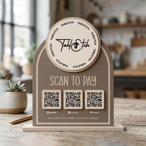 Puede incluir: Un letrero de pago arqueado de color topo con un logotipo circular con el texto Tabletch, las palabras SCAN TO PAY y tres códigos QR cuadrados para Venmo, Cash App y PayPal. La base es rectangular y de color beige claro.