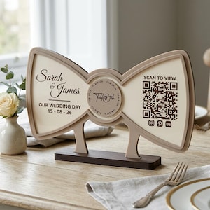 Könnte beinhalten: Ein fliegenförmiges Hochzeitsschild in Beige und Dunkelbraun. Die linke Seite zeigt den Text Sarah & James, OUR WEDDING DAY und 15-08-26. In der Mitte befindet sich ein kreisförmiges Tabletch-Logo. Rechts ist ein QR-Code mit SCAN TO VIEW zu sehen.