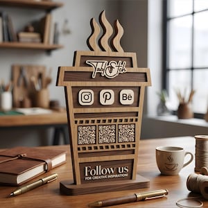 May include: A wooden display sign shaped like a coffee cup with steam rising from the top. It features the text TablEtch, social media icons for Instagram, Pinterest, and Behance, three QR codes, and the text Follow us FOR CREATIVE INSPIRATION!