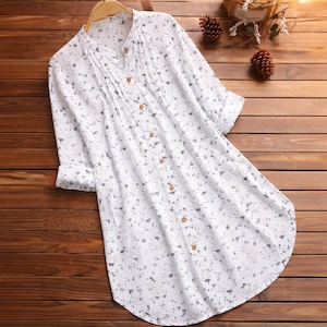Op de afbeelding: Witte tuniek-stijl blouse met een bloemenpatroon in grijstinten. De blouse heeft een opstaande kraag, een knoopsluiting en driekwartmouwen. De stof lijkt licht en geschikt voor warmer weer.