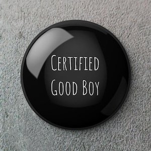 Könnte beinhalten: Ein glänzender, schwarzer runder Knopf mit dem weißen Text "CERTIFIED GOOD BOY". Der Knopf hat eine reflektierende Oberfläche. Der Hintergrund ist eine strukturierte, graue Oberfläche. Es ist wahrscheinlich ein Abzeichen oder ein Ansteck-Pin.