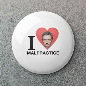 May include: A white button badge with the words "I MALPRACTICE" in black. A red heart shape contains a portrait of a man. The badge is circular and has a shiny surface.