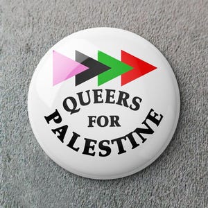 May include: A white button with the text "QUEERS FOR PALESTINE" in black, with a series of colored arrows. The arrows are pink, black, green, and red. The button is round and has a glossy finish.