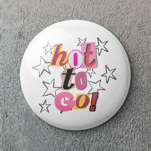 Puede incluir: Una chapa blanca con la frase "hot to go!" en un estilo collage, utilizando letras rosas, amarillas y rojas. El diseño se complementa con contornos de estrellas negras, creando una estética lúdica.