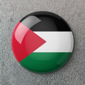 May include: A round button pin featuring the flag of Palestine. The pin has a glossy finish and displays the flag's colors: red, white, black, and green. The red triangle points towards the left, with the black stripe at the top.