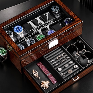 May include: A dark wood watch and accessory storage box with a glass lid featuring the text "W WILLIAMS". The top section holds multiple wristwatches, while the pull-out drawer contains compartments for rings, sunglasses, and various jewelry pieces.