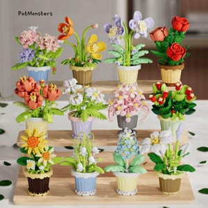 Può includere: Una collezione di colorate composizioni floreali in miniatura in piccoli vasi. I fiori includono rose, ortensie e girasoli, con foglie verdi. I vasi sono in vari colori, tra cui blu, giallo e marrone. Il testo "PotMonsters" è visibile.