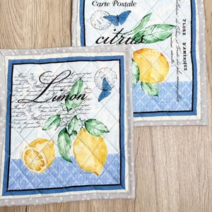 Peut inclure: Deux dessous de plat matelassés sur le thème du citron. Chacun présente une illustration de citron, des feuilles vertes et des papillons bleus. Les textes "citrus" et "Limon" sont visibles, ainsi que d'autres écritures. Les bordures sont bleues et grises.