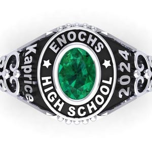 Può includere: Un anello di classe color argento con una grande pietra verde ovale al centro. L'anello presenta le scritte "Enochs High School 2024" e "Kaprice". L'anello ha decorazioni in filigrana sui lati.