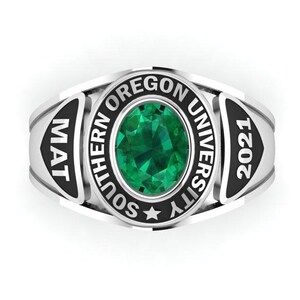 Peut inclure: Une bague de promotion argentée avec une grosse pierre verte ovale au centre. La bague porte les inscriptions "SOUTHERN OREGON UNIVERSITY" et "2021" en noir. La bague porte également les lettres "MAT" sur le côté.