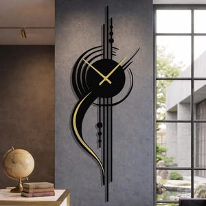 Puede incluir: Un gran reloj de pared moderno con esfera negra y manecillas doradas. El reloj presenta un diseño abstracto único con líneas negras y detalles dorados. Está montado en una pared gris en una habitación bien iluminada.