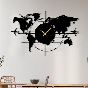 Puede incluir: Un reloj de pared de mapa del mundo de metal negro con manecillas doradas y dos siluetas de avión. El reloj tiene una esfera circular y líneas horizontales. El reloj está montado en una pared blanca sobre un mueble de madera con cestas tejidas.