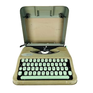 Könnte beinhalten: Vintage Schreibmaschine in Hellgrün und Beige. Die Tastatur hat hellgrüne Tasten mit weißer Beschriftung. Die obere Abdeckung ist geöffnet und gibt den Blick ins Innere frei. Die Schreibmaschine steht vor weißem Hintergrund.