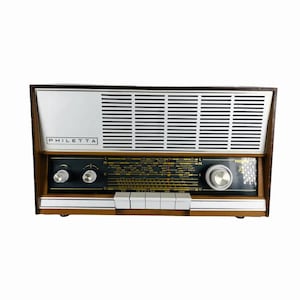 Op de afbeelding: Vintage Philetta-radio met een houten frame, zilveren luidsprekerrooster en zwart bedieningspaneel. De radio heeft knoppen, knoppen en een afstemknop. De merknaam "Philetta" staat op de voorkant.
