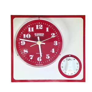 Puede incluir: Un reloj de cuarzo rojo con números y manecillas blancas, y un dial de temporizador blanco. La esfera del reloj tiene el texto "BLESSING ELECTRONIC" y "West-Germany". El reloj está en un marco blanco con un borde rojo.