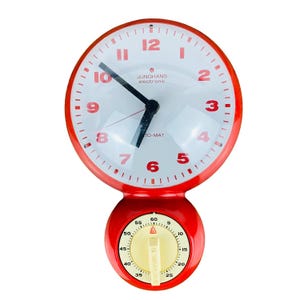 May include: A vintage red and white Junghans electronic TO-MAT kitchen timer and clock. The clock face has red numerals and hands. The timer has a yellow dial with a red indicator. The clock and timer are attached.
