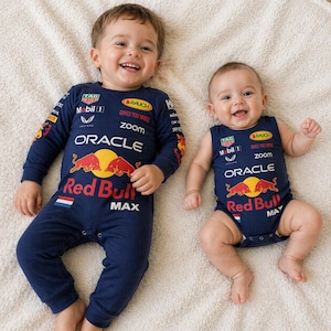 Könnte beinhalten: Zwei Babys in marineblauen Red Bull-Rennoutfits. Eines trägt einen langärmeligen Overall, das andere einen ärmellosen Body. Beide Outfits zeigen das Red Bull-Logo, Sponsorenlogos und das Wort "MAX".