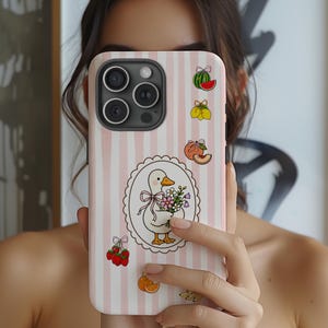 May include: A pink and white striped phone case featuring a cartoon duck holding flowers. The case has fruit illustrations and a decorative oval frame. The phone case is held in front of a person.