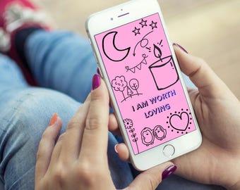 Może przedstawiać: Biały smartfon z różowym ekranem, na którym widnieją czarne rysunki liniowe przedstawiające półksiężyc, gwiazdy, świecę, drzewa i serce, wraz z tekstem "I AM WORTH LOVING" wydrukowanym na środku wyświetlacza.