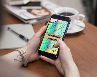 Może przedstawiać: Czarny smartfon wyświetlający grafikę cyfrową z holograficznym tłem, czarnymi rysunkami piór, gwiazd i misia oraz centralnym beżowym banerem o fakturze papieru z czarnym napisem I AM BECOMING STRONGER.