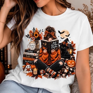 May include: A white t-shirt featuring a graphic of a person reading a book titled Just One More Chapter. The illustration includes a stack of books labeled Fantasy, Dark Romance, Thriller, Mystery, and Spicy Reads, a black cat, a ghost, and pumpkins.