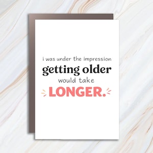Puede incluir: Una tarjeta de felicitación blanca con un borde marrón. La tarjeta presenta el texto "i was under the impression getting older would take LONGER." en letras negras y coral.