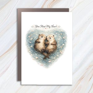 May include: A white greeting card featuring a watercolor illustration of two brown otters floating in blue water shaped like a heart. The otters are holding hands, and the text "You Float My Heart" is printed in black above the heart shape.