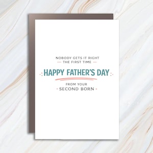 May include: A Father's Day greeting card with a white background and a brown border. The card reads "NOBODY GETS IT RIGHT THE FIRST TIME" and "HAPPY FATHER'S DAY" in a playful font. The message continues, "FROM YOUR SECOND BORN."