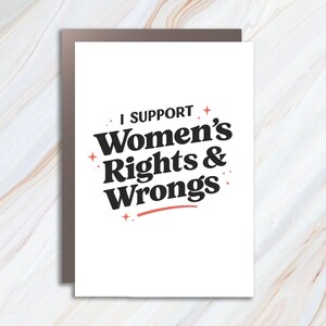 May include: A white greeting card with the text "I Support Women's Rights & Wrongs" in black, with red accents. The card is set against a marble-patterned background.