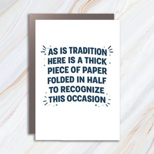 May include: A white greeting card with the text "AS IS TRADITION HERE IS A THICK PIECE OF PAPER FOLDED IN HALF TO RECOGNIZE THIS OCCASION" in navy blue. The card is inside a brown envelope.