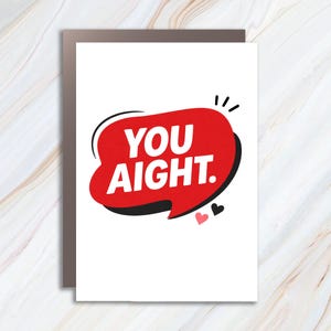 May include: A greeting card with the text "YOU AIGHT." in white letters inside a red speech bubble with a black outline. Two small hearts, one pink and one black, are below the bubble. The card is on a white background.