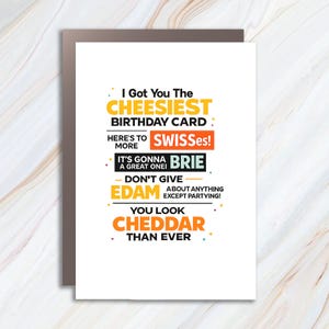 Könnte beinhalten: Eine weiße Geburtstagskarte mit braunem Rand. Die Karte enthält farbenfrohen Text mit der Aufschrift "I Got You The Cheesiest Birthday Card" und andere Wortspiele zum Thema Käse. Die Karte ist humorvoll gestaltet.